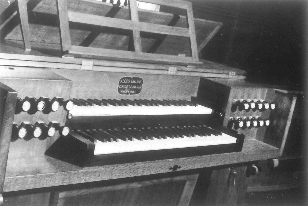 Der Spieltisch der Orgel in der Pfarrkirche. Auf einer Plakette ist folgendes zu lesen: „ALOIS ERLER – ORGELBAUER – FECIT 1851“. schwarz-weiß.